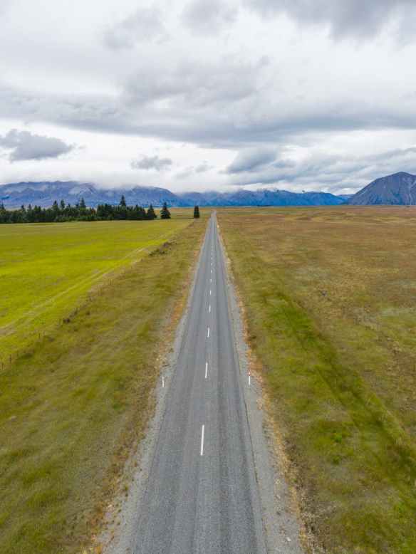 gray asphalt road between green grass field